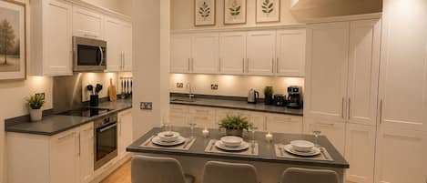 Une cuisine moderne avec des meubles blancs, un îlot central doté de tabourets de bar et une table à manger pour quatre personnes.