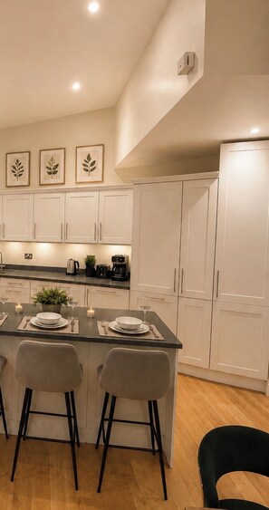 A modern kitchen with white cabinets, a central island with bar stools, and a dining area with a table set for two. - Mr Marylebone · Stylish 3BR Home · Sleeps 6 (London)