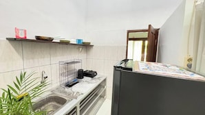 A kitchen with a sink, a refrigerator, a microwave, and a shelf with dishes and a bag of sugar. - Pondok Cintya Kerobokan Canggu (Badung)