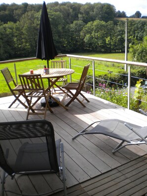 A deck with a table and chairs, an umbrella, and a view of a green landscape. - Le Chênelierre - Everything for the Kids - Dogs Welcome (Free) (Manhay)