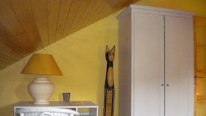 Ein Zimmer mit einem weißen Schrank, einem Korbstuhl, einer Lampe und einem dekorativen Gegenstand.