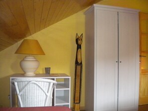 A room with a white cabinet, a wicker chair, a lamp, and a decorative item. - Le Chênelierre - Everything for the Kids - Dogs Welcome (Free) (Manhay)