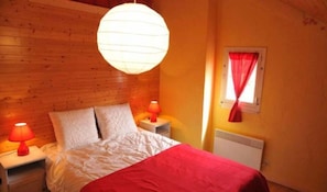 A bedroom with a wooden headboard, a bed with white bedding, a red throw, two bedside lamps, and a window with a red curtain. - Le Chênelierre - Everything for the Kids - Dogs Welcome (Free) (Manhay)
