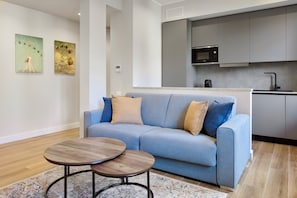 Ein modernes Wohnzimmer mit einer Couch, zwei Couchtischen und einer Küche im Hintergrund.