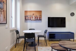 Ein modernes Wohnzimmer mit einem runden Esstisch, schwarzen Stühlen, einem Flachbildfernseher, einer blauen Unterhaltungsanlage und einem großen Gemälde an der Wand.