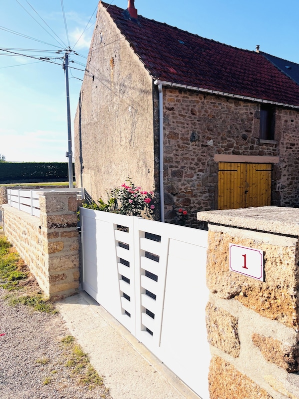 A stone building with a red-tiled roof, a wooden door, and a white gate.