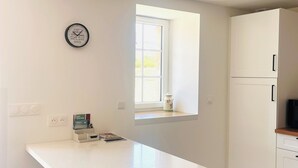 A kitchen with a white countertop, a window, and a clock on the wall. - Our traditional house with an enclosed courtyard, 3 km from the sea (Carneville)