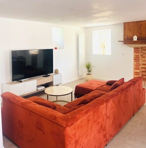 A modern living room with a large flat-screen TV, a sofa set, a small round coffee table, and a potted plant.