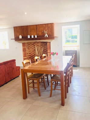 A dining area with a wooden table and chairs, a brick fireplace, and a red sofa.