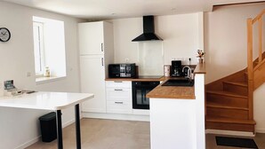 A modern kitchen with white cabinetry, a black range hood, and a wooden staircase. - Our traditional house with an enclosed courtyard, 3 km from the sea (Carneville)