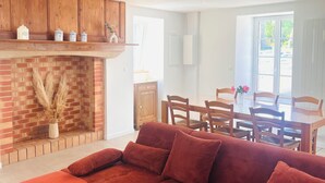 A living room with a red sofa, a round coffee table, and a brick fireplace. - Our traditional house with an enclosed courtyard, 3 km from the sea (Carneville)