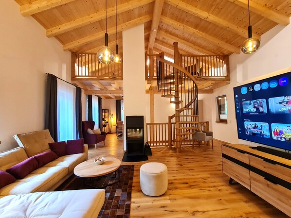 A spacious living area with a wooden floor, a sofa, a coffee table, a TV, and a staircase. - Chalet Rehblick (Bad Kleinkirchheim)