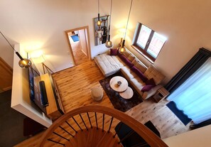 A spacious living area with a wooden floor, a sofa, a coffee table, and a staircase leading to another level.