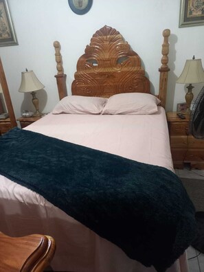 Uma cama com cabeceira de madeira, duas mesas de cabeceira com abajures e um cobertor azul-escuro.
