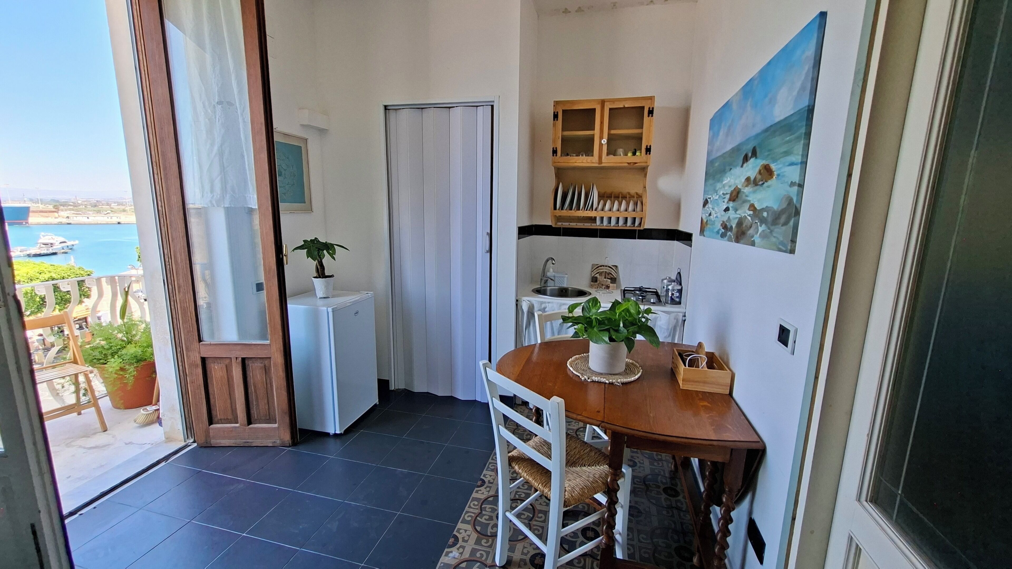 A compact kitchen with a dining area, a small refrigerator, and a view of the sea.