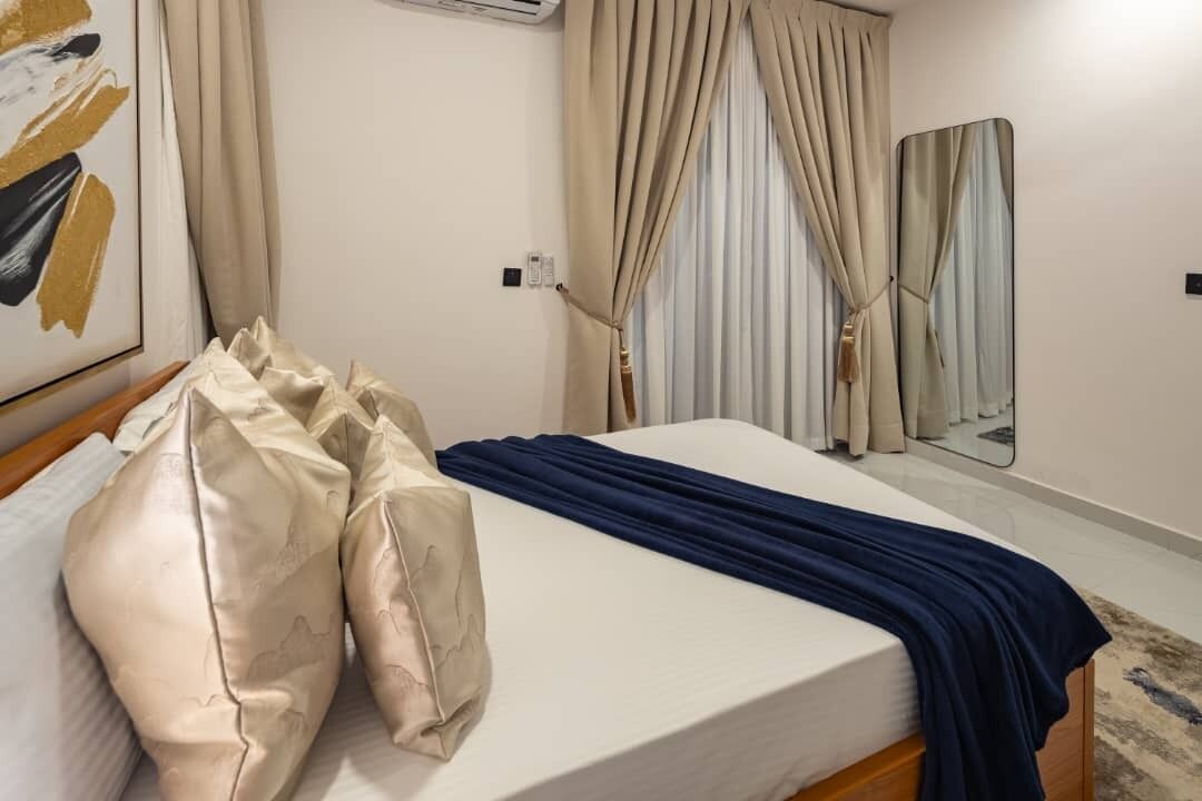 Une chambre d’hôtel avec un lit, des rideaux beiges, un miroir et un tableau au mur.