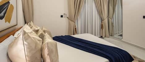 A hotel room with a bed, beige curtains, a mirror, and a painting on the wall.