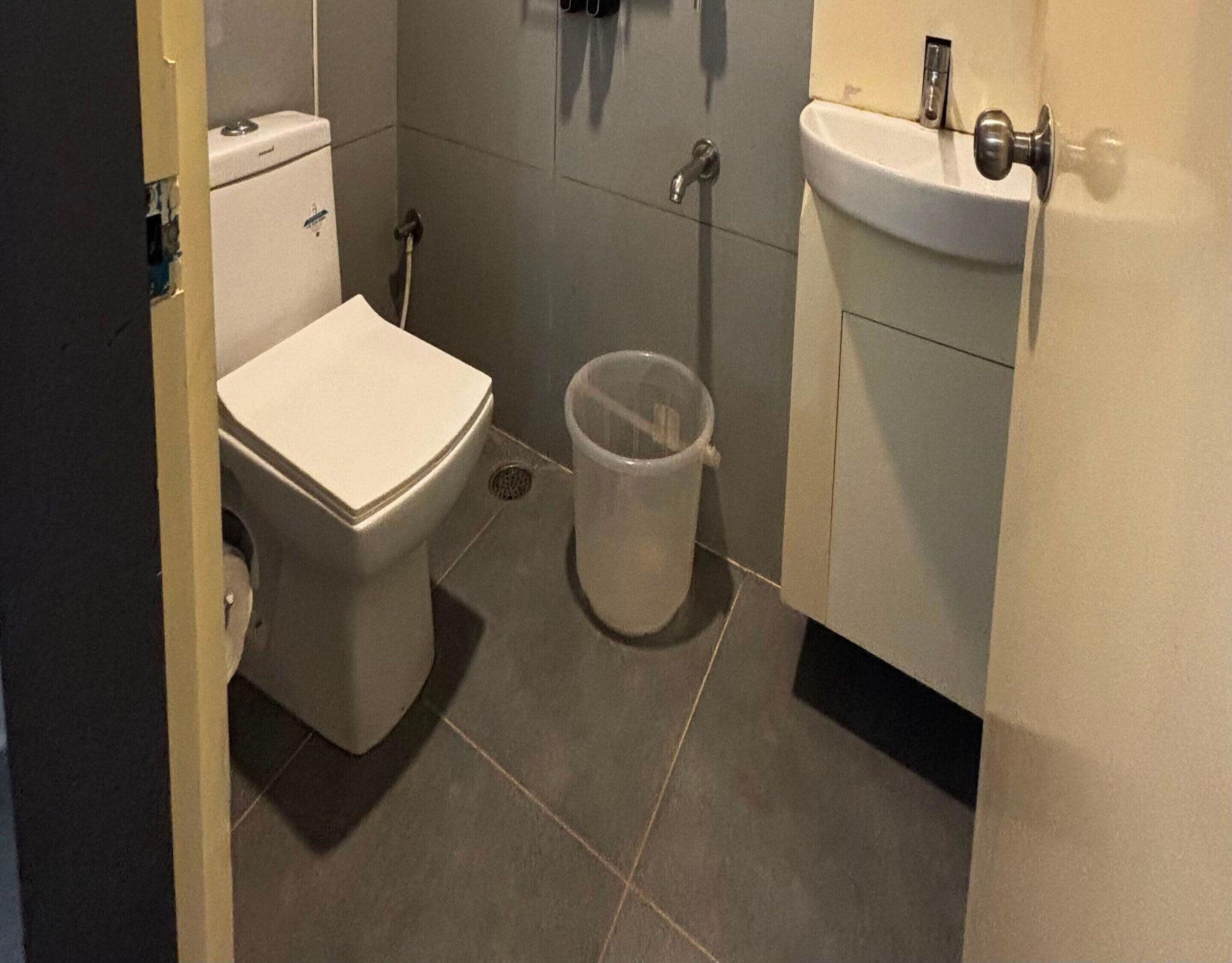 A small bathroom with a toilet, a sink, and a trash bin.