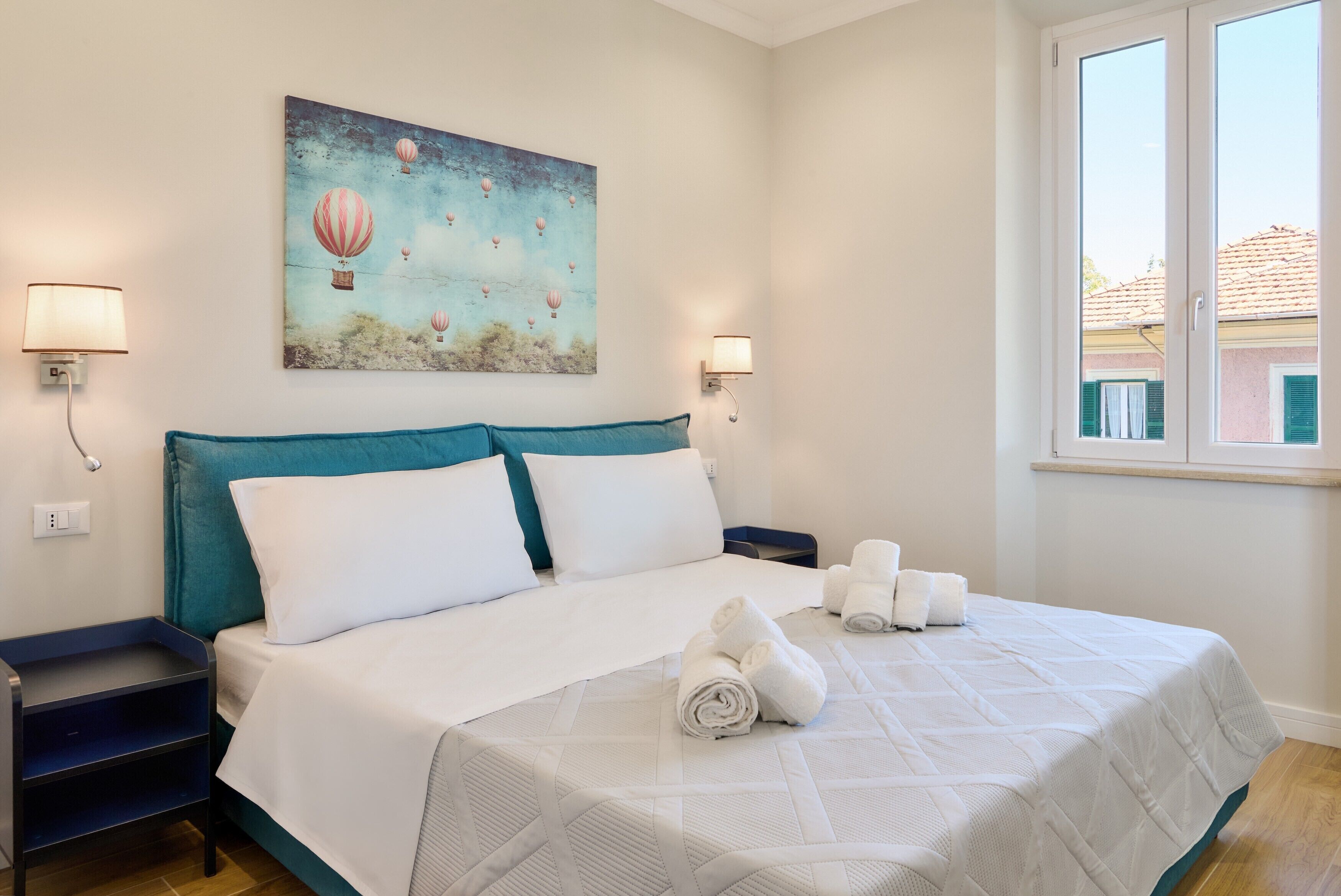 A hotel room with a bed, two bedside tables, a painting, and a window.