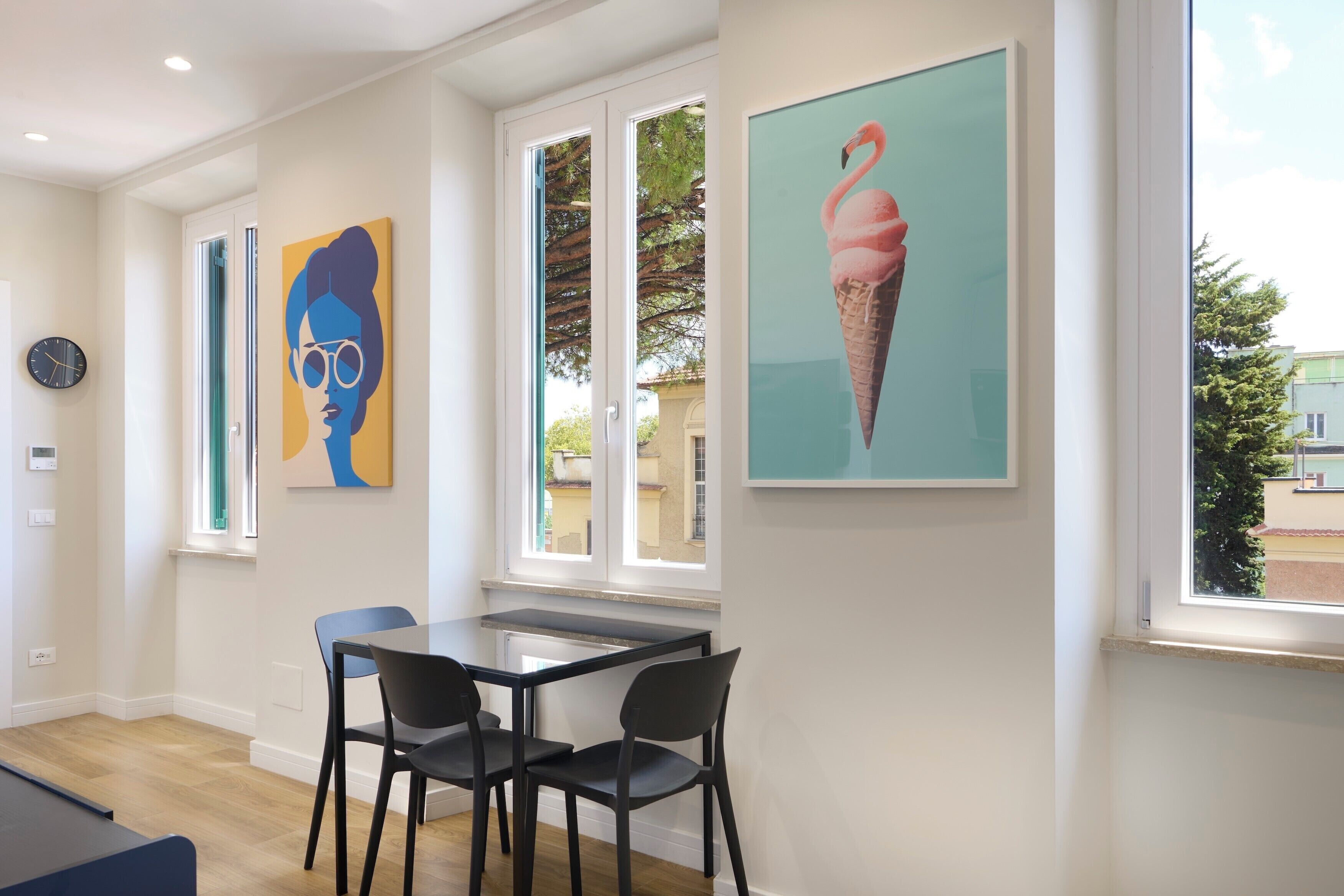 A room with a dining table, two chairs, a clock, and artwork on the walls.
