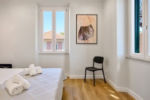 Un dormitorio con una cama, una silla, un ventanal y un cuadro.