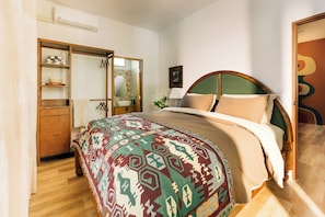 Un dormitorio con cama, armario, espejo y una puerta que da a otra habitación.