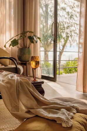 Una habitación con una cama, una mesa de vidrio con una vela, una planta en maceta y vista a zonas verdes al exterior.