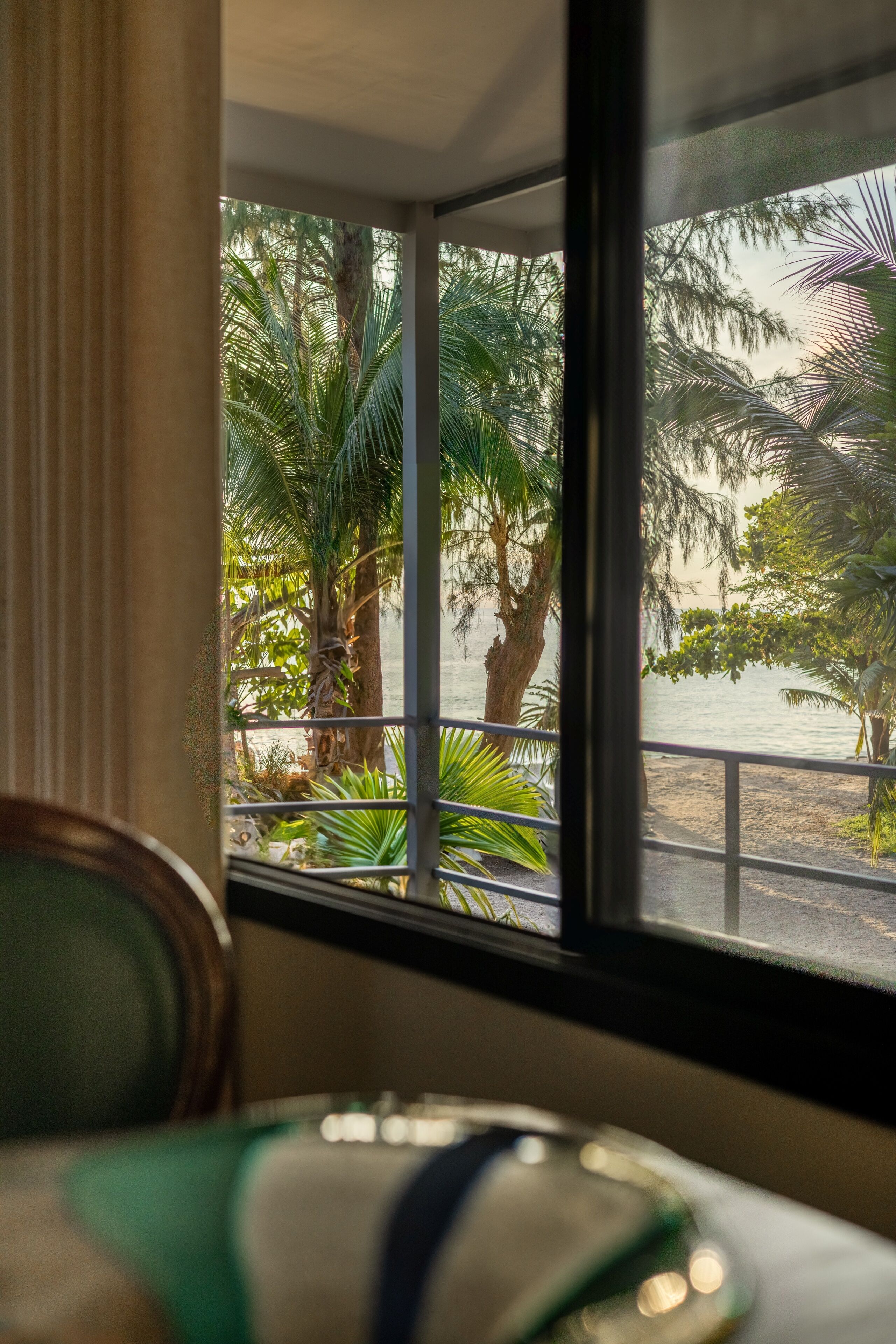 Ein Zimmer mit Blick auf einen Strand und Palmen durch ein Fenster.