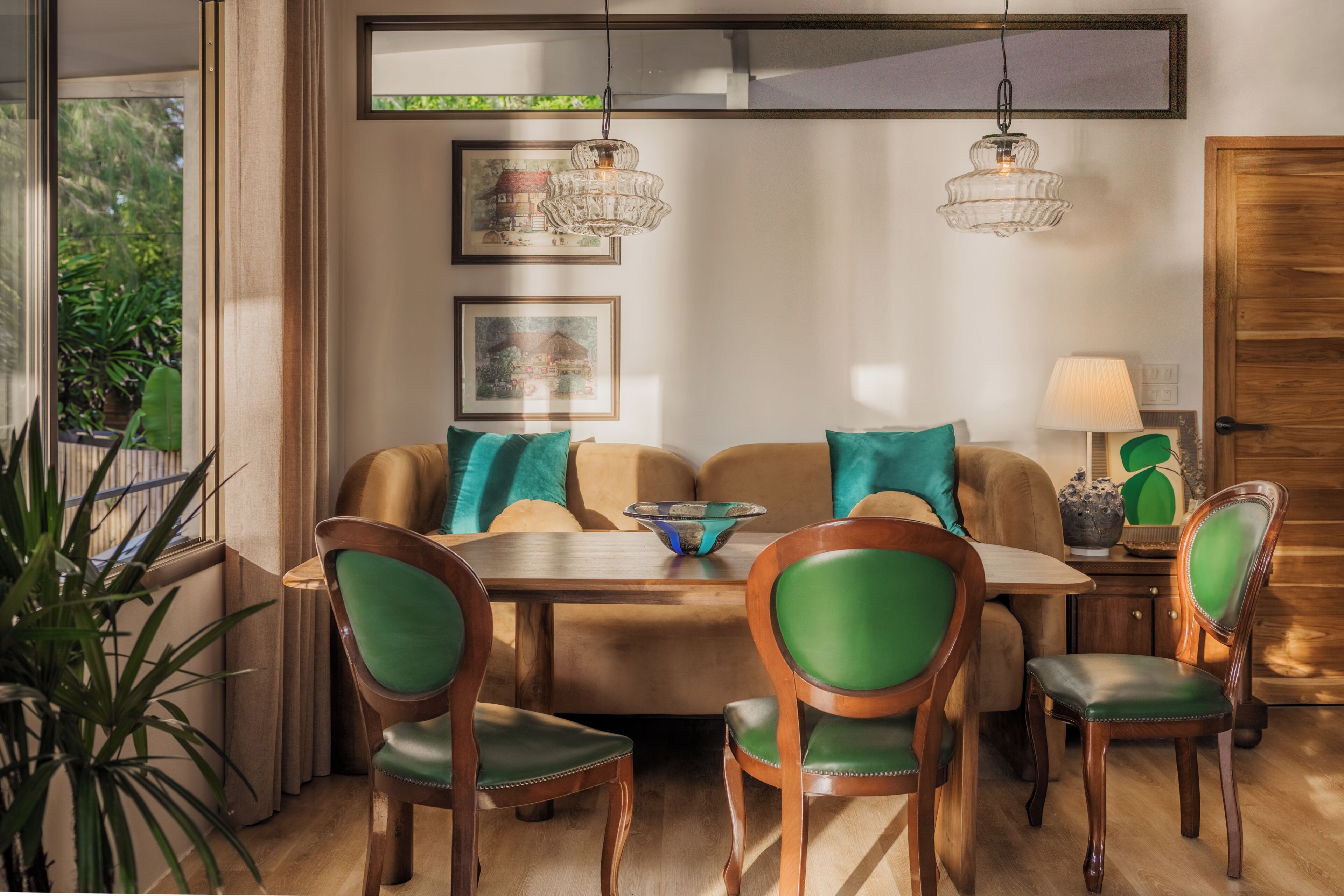 Un comedor moderno con una mesa de madera, sillas tapizadas en verde y dos lámparas colgantes.