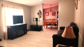 Una sala de estar con televisor, sofá, mesa de centro y un comedor con sillas y mesa.