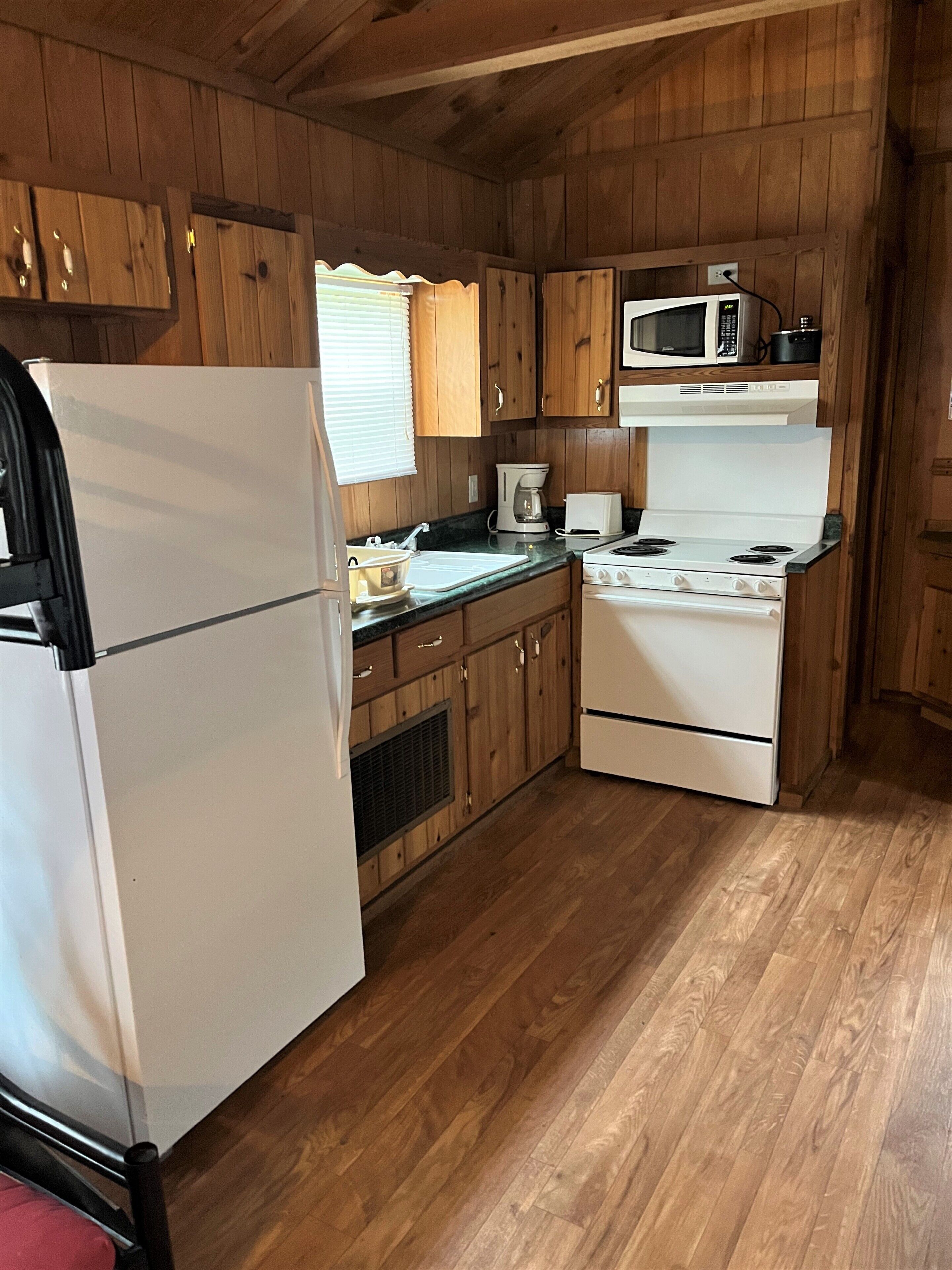 A compact kitchen with wooden cabinets, a white refrigerator, a microwave, a stove, and a coffee maker.