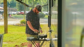 A person ironing clothes outdoors with a portable ironing board. - Pin Oak RV Resort (Villa Ridge)