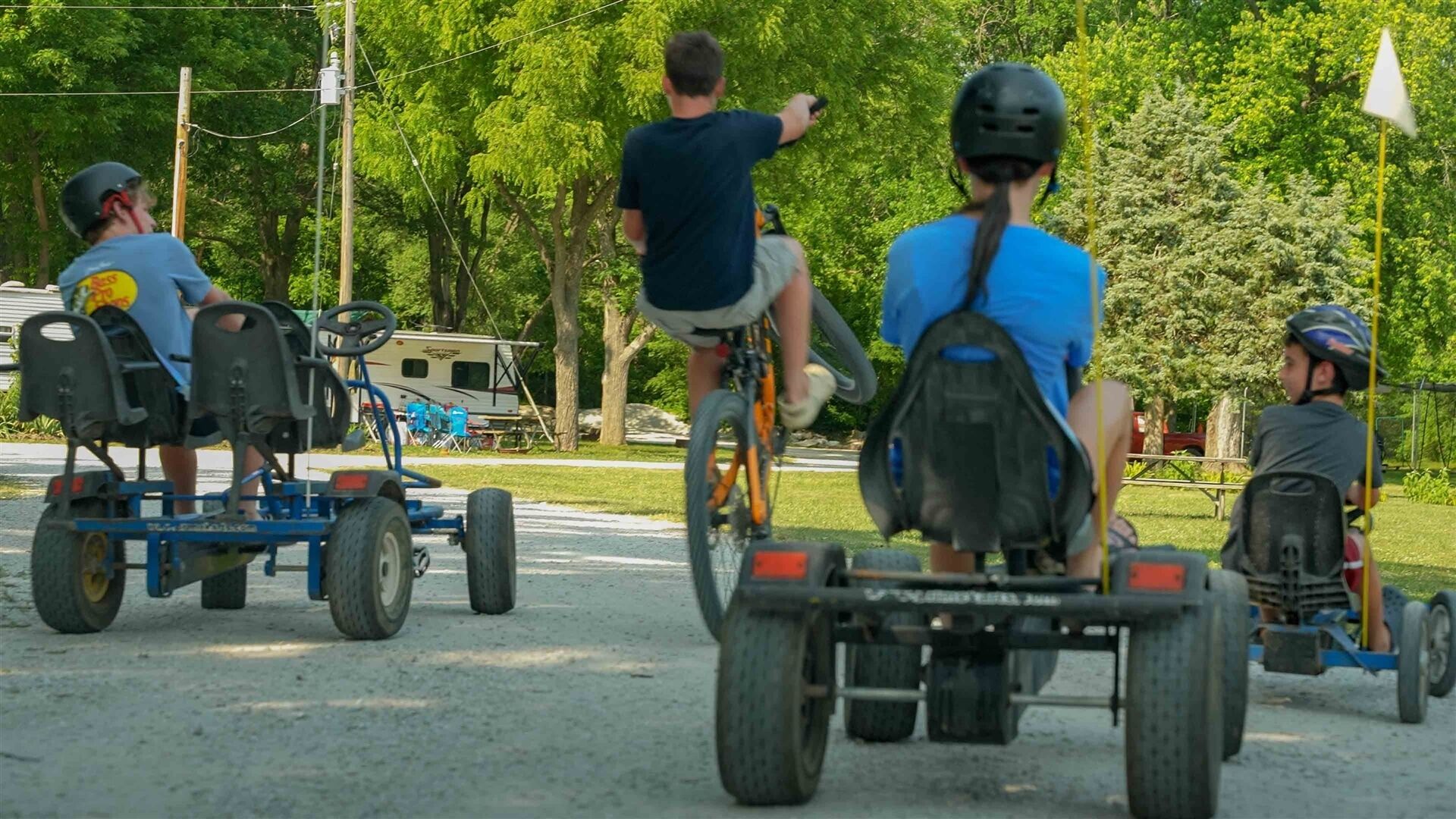 Un gruppo di persone su una pista di go-kart, con un rimorchio, circondati da alberi e un campeggio sullo sfondo.