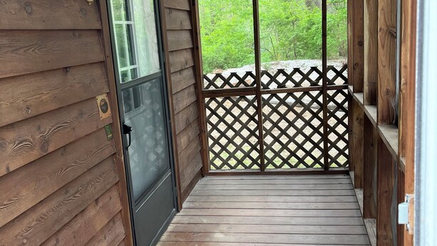 Una terraza de madera con un cerramiento de celosía y una puerta que da a una zona cubierta.