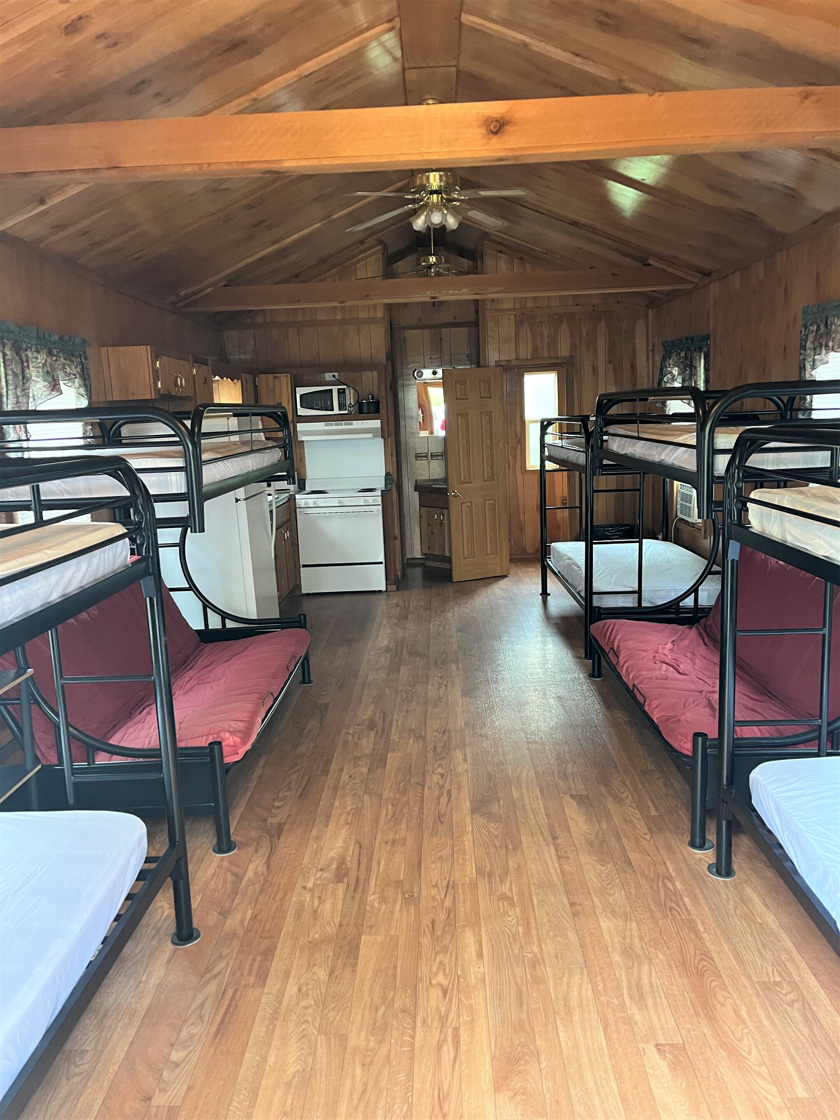 A cabin interior with bunk beds, a kitchenette, and a ceiling fan.