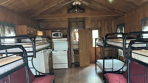 Interior de una cabaña con literas, kitchenette y ventilador de techo.