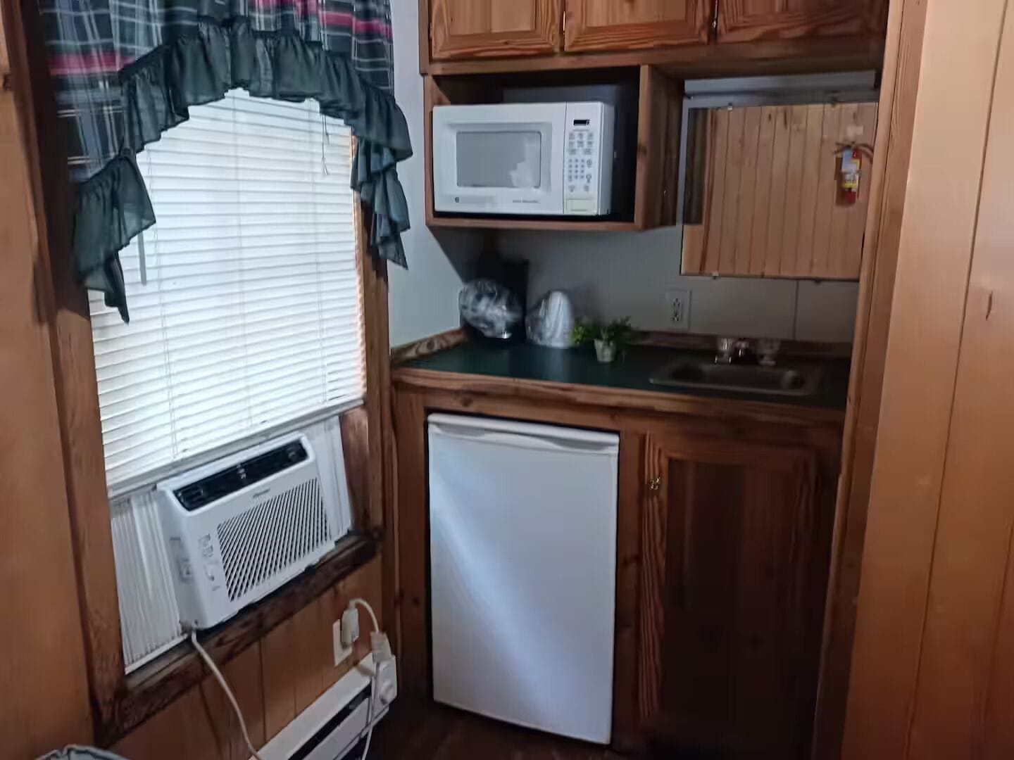 A compact kitchen with a microwave, a small refrigerator, and a window with blinds.