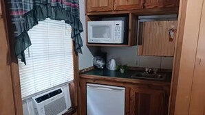 Una cocina compacta con microondas, un refrigerador pequeño y una ventana con persianas.