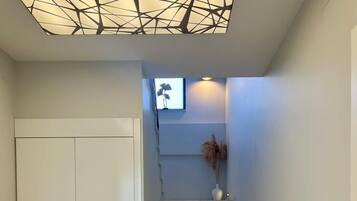 A staircase with a geometric ceiling design, a white wardrobe, and a vase with dried plants.