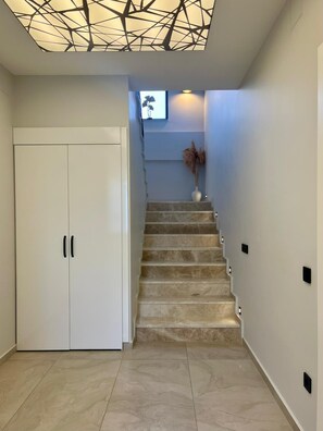 Eine Treppe mit einem geometrischen Deckendesign, ein weißer Kleiderschrank und eine Vase mit Trockenpflanzen.