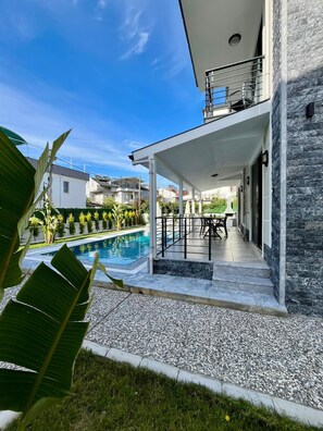 A modern house with a swimming pool, a covered patio, and a stone exterior.