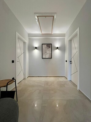 Ein Korridor mit modernem Design, der ein gerahmtes Kunstwerk an der Wand, zwei Wandleuchten und eine Deckenleuchte zeigt.