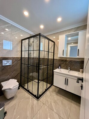 A modern bathroom with a glass-enclosed shower, marble walls, and white cabinetry.