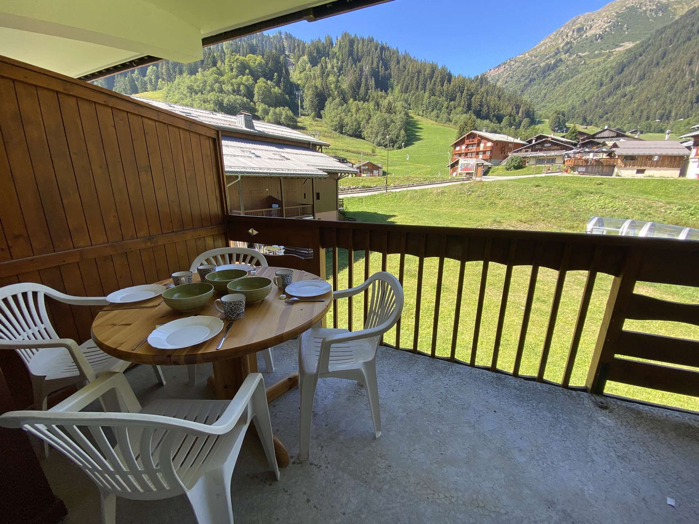 Un balcón con mesa lista para comer, con vistas a un paisaje montañoso con edificios tradicionales.