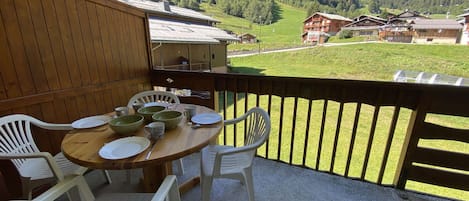 Un balcón con mesa lista para comer, con vistas a un paisaje montañoso con edificios tradicionales.