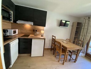 A compact kitchen with a microwave, coffee maker, and a small refrigerator. There is a dining table with chairs and a flat-screen TV mounted on the wall. - Cozy apartment - 4 guests at the foot of the slopes (Arêches-Beaufort)