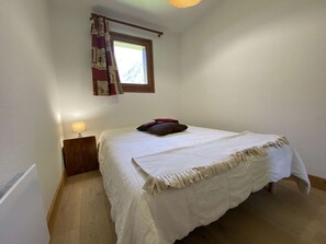 A bedroom with a bed, a nightstand, a lamp, and a window with curtains. - Cozy apartment - 4 guests at the foot of the slopes (Arêches-Beaufort)