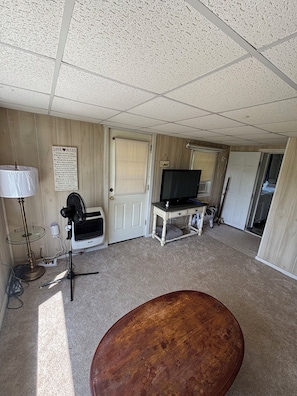 Una habitación con televisión, lámpara, ventilador y un banco de madera.