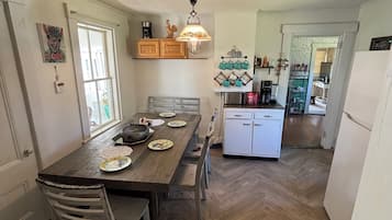 A kitchen with a wooden dining table, chairs, a hanging light fixture, and a refrigerator.