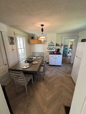 Una cocina con una mesa de comedor de madera, sillas, una lámpara colgante y un refrigerador.